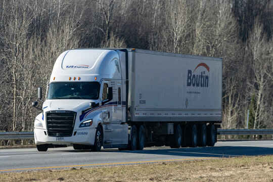Quebec, Canada, 24 April 2026 : A TJS Express semi-truck with a Boutin trailer drives on a highway past bare trees.