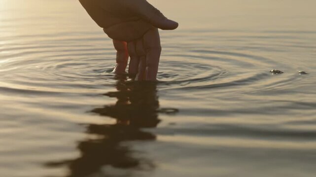 Lowering human hand after bubble surfacing, touching water at sunset, creating ripples, copy space