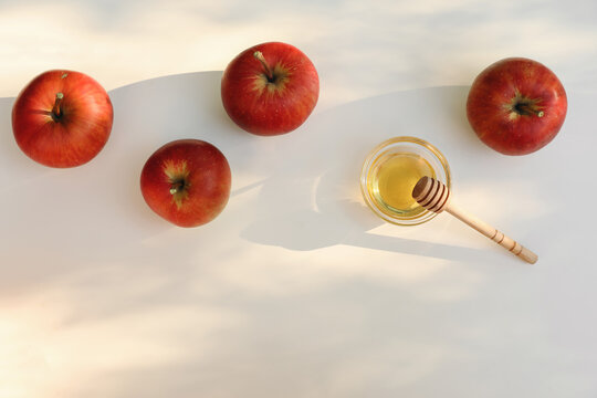Rosh Hashanah apples and honey with wooden honey dipper on white background in warm natural sunlight, traditional Jewish New Year holiday food with copy space. Autumn harvest Flat lay, top view.