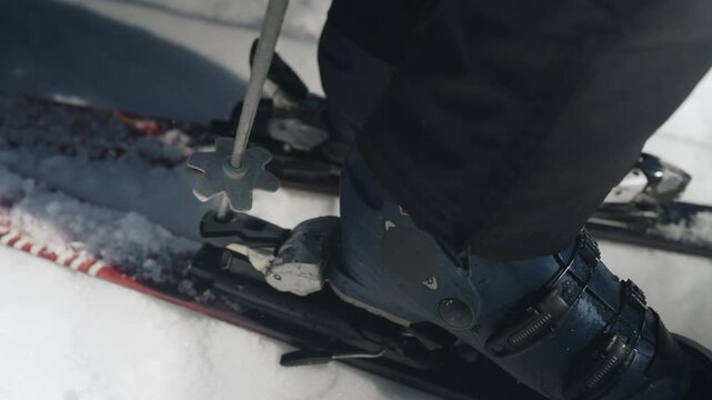 A person prepares for winter sport, clipping ski boots into bindings. They are also seen disengaging from skis in fresh snow.
