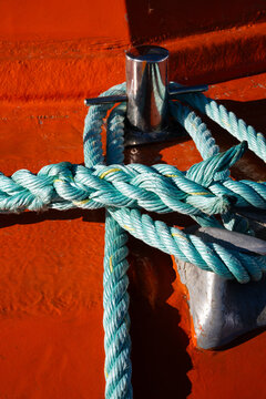 Turquoise mooring rope wrapped around stainless steel boat cleat on weathered red deck creating a nautical texture background