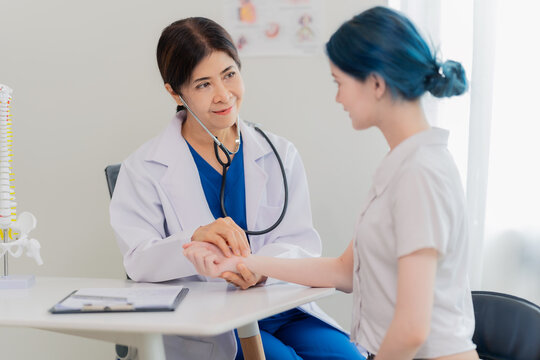 Senior female doctor checking young patient's pulse rate on wrist during medical examination.