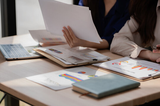 Close up of businesswomen working together analyzing data reports and graphs on wooden desk.