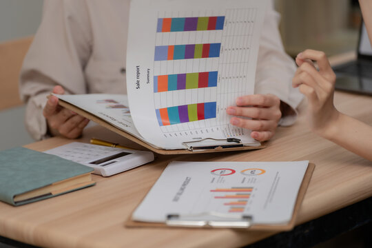 Close up of businesswomen working together analyzing data reports and graphs on wooden desk.