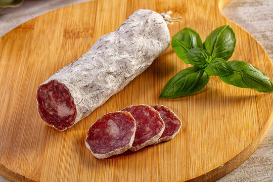 Traditional dry cured salami sausage with fresh basil leaves on a round wooden board