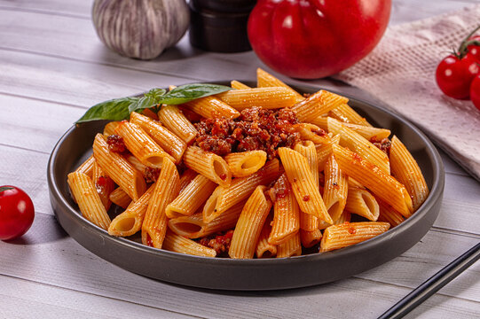 Penne pasta with bolognese sauce and fresh basil on rustic wooden table
