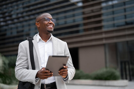 Black businessman working as sales manager, using tablet, reviewing chart, outdoor near office building. African american business man smiling, prepared for client meeting, growing network. Copy space