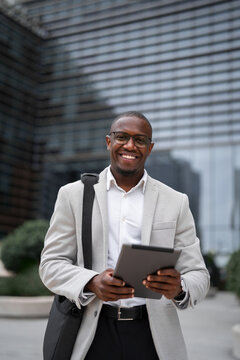 Using tablet, presenting data, black businessman outdoor near office building, works as marketing director, vertical. African business man smiling, ready for next meeting, managing accounts.