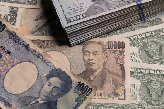 Japanese yen banknotes surrounding stack of US 100 dollar bills