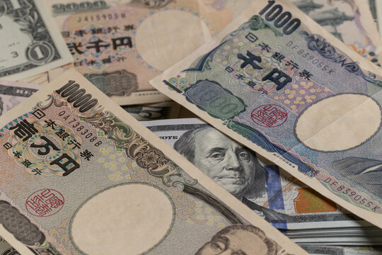 Japanese yen banknotes surrounding stack of US 100 dollar bills