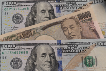 Japanese 10000 yen banknote placed between US 100 dollar bills