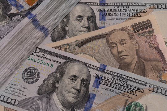 Japanese 10000 yen bill placed between US 100 dollar banknotes next to money stack