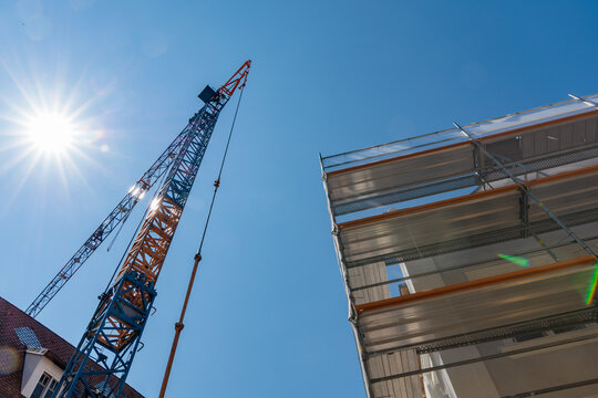 Low angle view of tall construction crane and metal scaffolding against bright sun starburst and clear blue sky on site