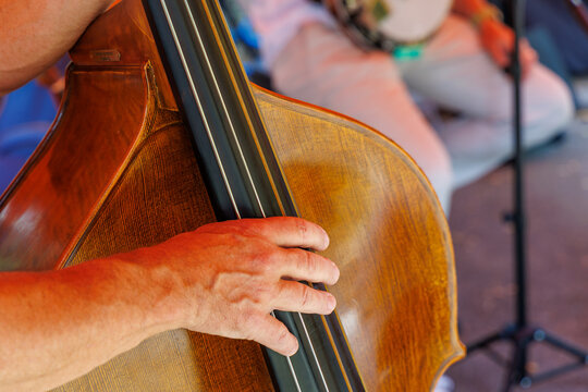 Close up of musician hand playing wooden double bass on stage during live concert performance with blurred banjo player in background