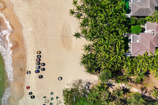 Numerous traditional basket boats rest on the shore and near the gentle waves of the clear ocean