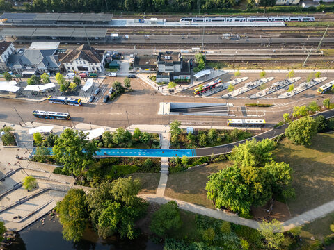 Aerial view of the Tubingen Hauptbahnhof train station with railway tracks, buses, a blue bicycle path, and surrounding green park areas, Tubingen, Baden-Wurttemberg, Germany.