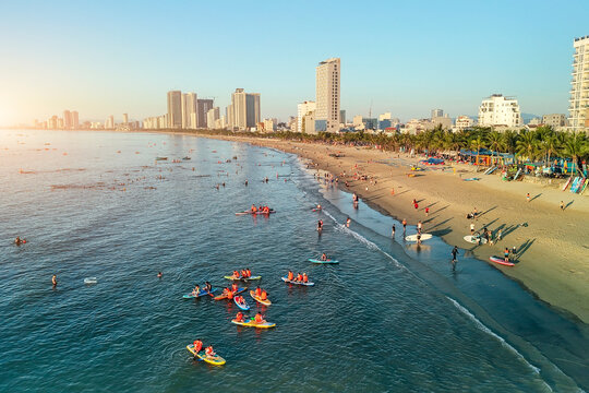 Beachgoers swim and paddle on paddleboards and surfboards in the vibrant blue ocean along Da Nang busy shoreline