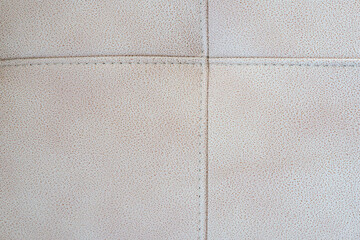 Obraz premium Close-up of a beige tufted leather upholstery texture with stitched crossed seams