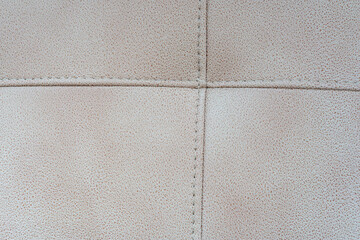 Fototapeta premium Close-up of a beige tufted leather upholstery texture with stitched crossed seams