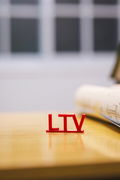 Red ltv letters on a wooden desk with a rolled blueprint in a blurred office setting, planning and business concept