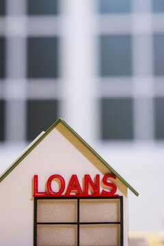 Small model house with the word loans on the roof, with a blurred building background