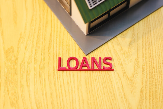 House model with the word loans on a wooden table, mortgage and home financing concept