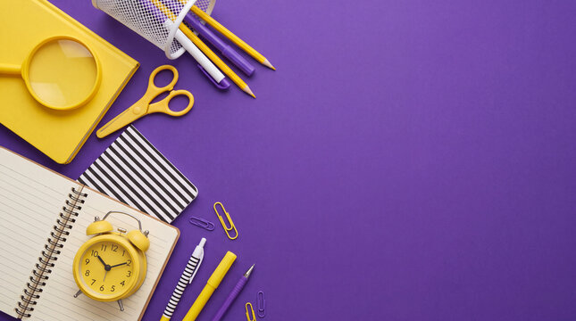 Top view flat lay of yellow school and office supplies including notebooks, a clock, scissors, and pens arranged on a vibrant purple background with copy space.