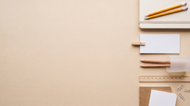 Flat lay workspace mockup with empty blank notebooks, wooden pencils, ruler, and paper clips aligned on beige background with copy space. Modern office, education, and branding composition.