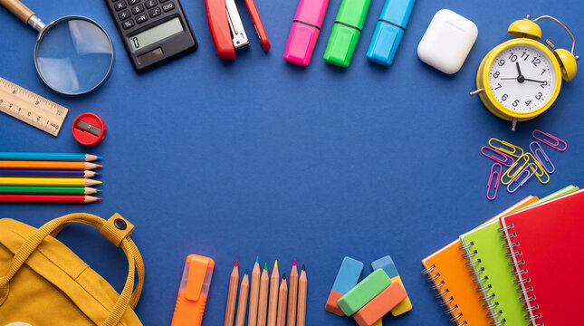 Flat lay top view frame of colorful school and office supplies with empty copy space on a vibrant blue background. Perfect for back to school sale banners, education templates, and learning concepts.