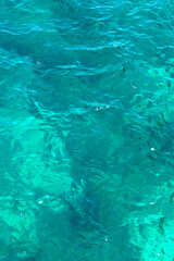 Clear turquoise sea water with gentle waves and sunlight reflections. Natural ocean surface texture as a summer, tropical vacation or marine background with copy space © Anastasiia