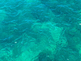 Clear turquoise sea water with gentle waves and sunlight reflections. Natural ocean surface texture as a summer, tropical vacation or marine background with copy space © Anastasiia