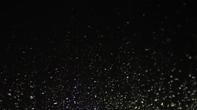 Multiple tiny raindrops cover the glass surface against a completely dark background. Low side lighting makes the moisture shimmer, creating a dense macro texture of night rain