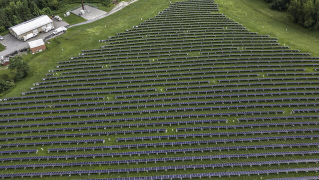 Aerial view of rows of solar panels installed in a grassy field with a nearby maintenance building in Patterson, New York, United States.