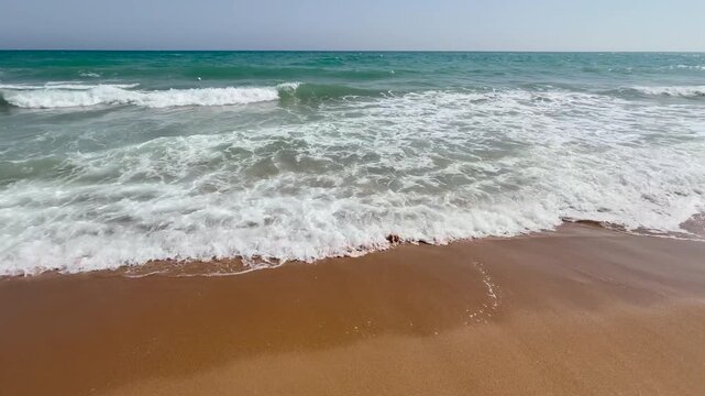 Breaking Mediterranean waves washing onto a sandy beach on a sunny summer day in Sicily, Italy. Clear sea, blue sky and relaxing coastal scenery with gentle camera movement.