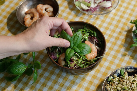 Making seasonal summer salad with shrimp. Hand decorating salad with basil. Heathy dinner. 
