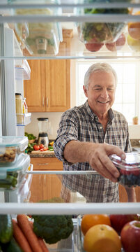 Smiling senior man choosing fresh berries from organized refrigerator full of produce, authentic active aging concept showing independence value value value value value value value