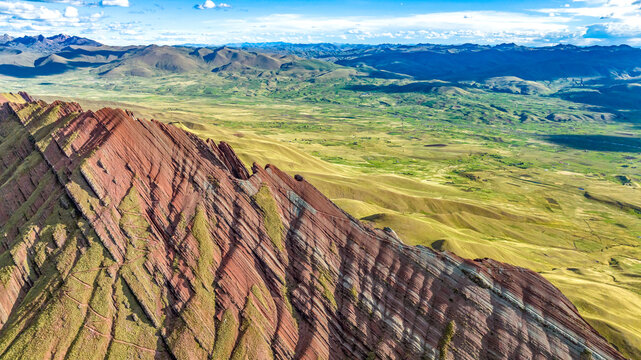 Aerial view of the colorful striped rock formations of Vinicunca, also known as Rainbow Mountain, set against the vast Andean landscape in Quispicanchi Province, Cusco, Peru.