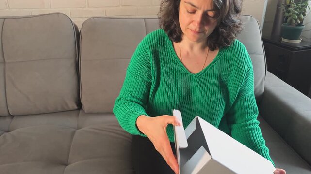 Woman unwraps a gift box in living room while sitting on couch