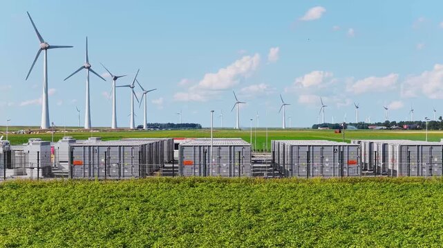 Aerial view of battery energy storage system facility next to wind turbines. Industrial lithium battery system for renewable power plant and grid management.