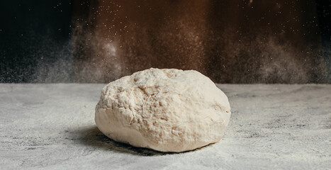 Obraz premium Raw dough ball covered in flour sits on a wooden surface with a dusting of flour in the background, ideal for baking and culinary preparation