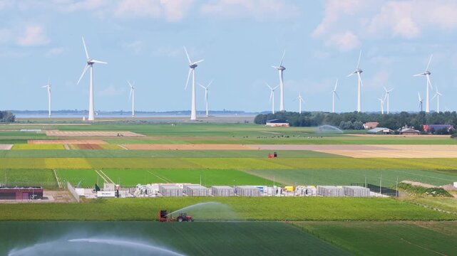 Aerial drone view of agricultural field with crop rows and irrigation system. Wind turbines generating green energy on background of farmland.