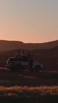 Travellers on a 4x4 at sunset, Namibia. Aerial view of a group on the roof of a vehicle above the Sossusvlei hills.