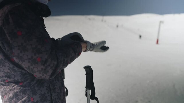 A person in full ski gear, including a unique frog helmet and goggles, prepares on a snow-covered mountain. The individual adjusts their gloves and eyewear, ready for winter sports and adventure.