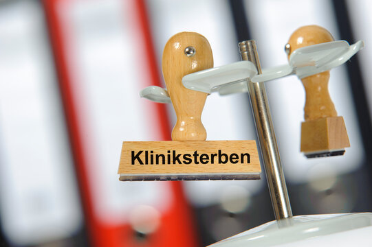 In einem B&uuml;ro mit Aktenordner h&auml;ngt ein Holzstempel mit der Aufschrift: Kliniksterben