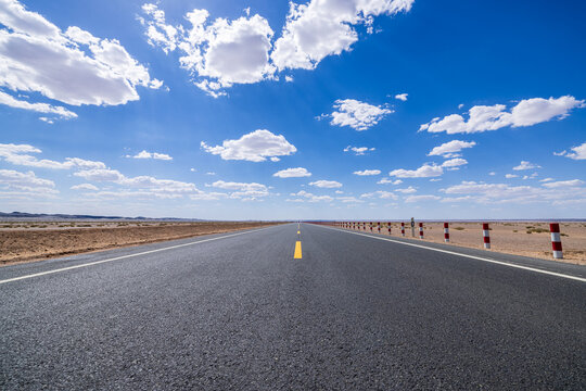 Empty straight asphalt highway stretching to the horizon through a desert landscape under a blue sky with clouds