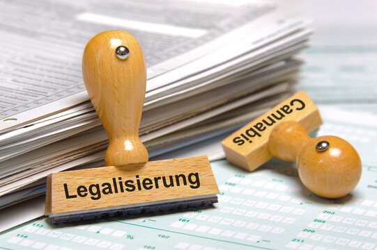 An einem Stapel mit Formularen lehnt ein Holzstempel mit Aufdruck Legalisierung von Cannabis