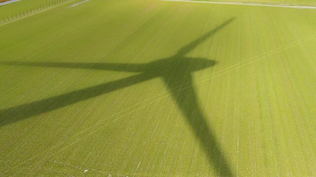 Aerial drone view of agricultural field with crop rows. Rotating shadow of a wind turbine blade moving across farmland on a sunny day.
