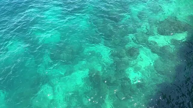 Clear turquoise sea water with gentle waves and sunlight reflections. Natural ocean surface texture as a summer, tropical vacation or marine background with copy space