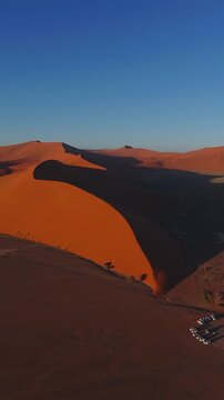 Red dunes of Sossusvlei, Namibia. Aerial view along a towering sand ridge with hikers small against the sunlit slope.