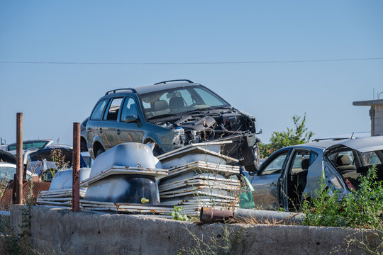 a heavily dismantled blue station wagon sitting elevated among a pile of discarded bathtubs and scrap materials in an outdoor auto salvage yard.